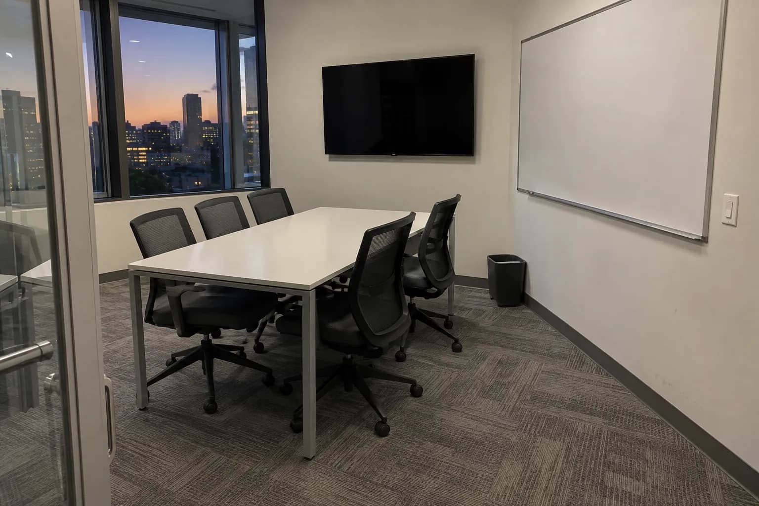 A small glass-walled meeting room with the table cleared and chairs pushed in